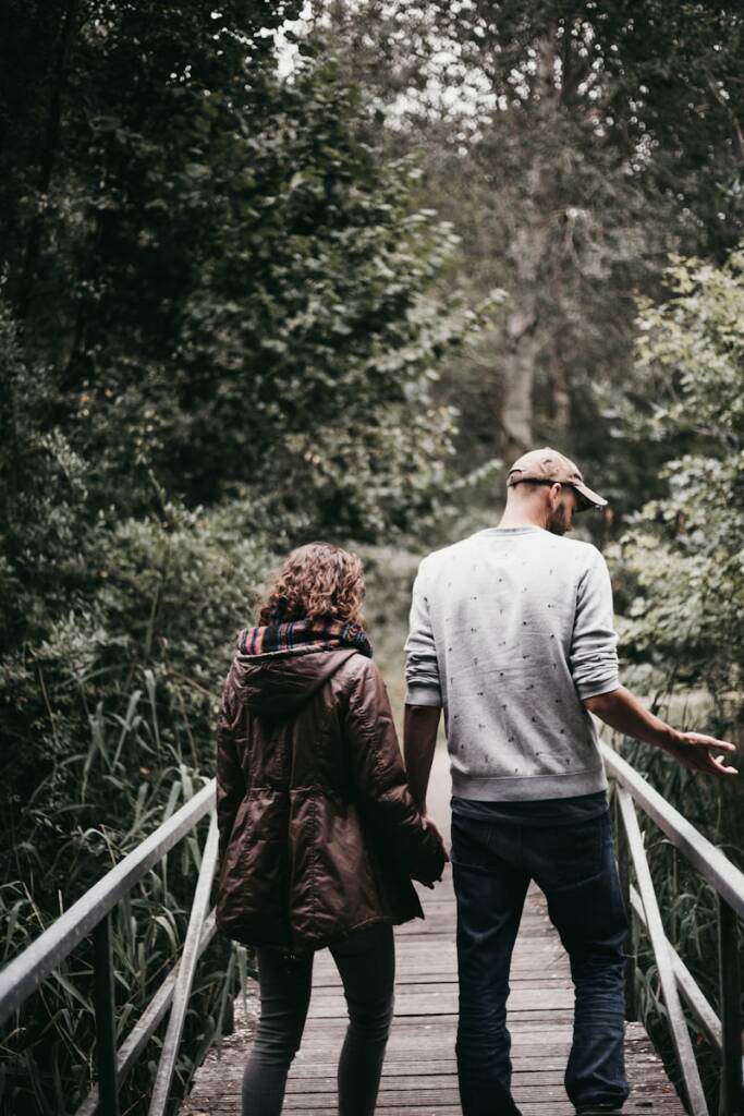 man and woman holding hands walking on bridge during daytime