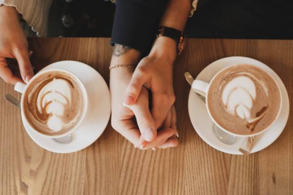 two people holding hands beside white ceramic coffee cups