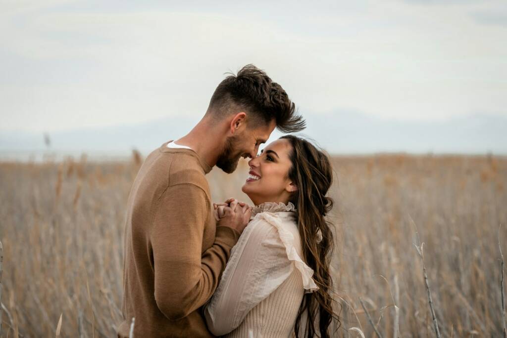 Couple looks at each other lovingly in a field.