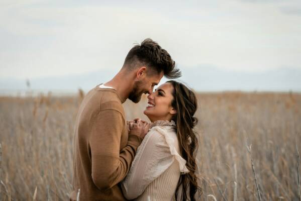 Couple looks at each other lovingly in a field.