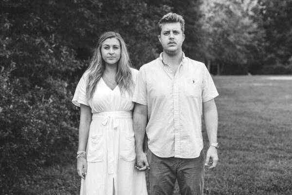 grayscale photo of man and woman standing on grass field