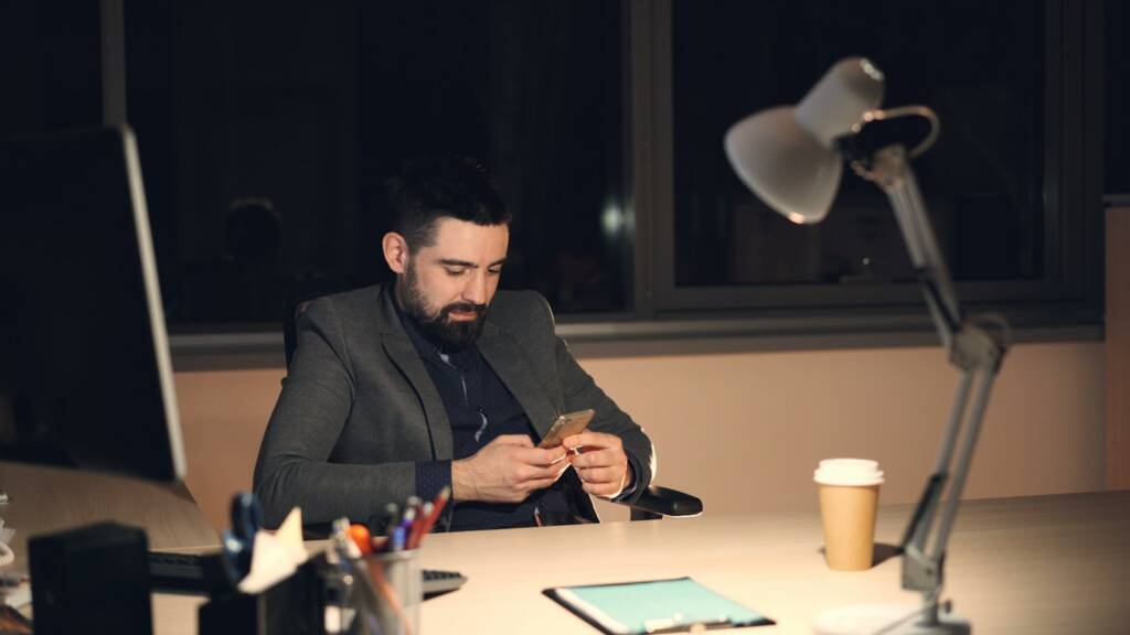 Man working late on his phone at desk.