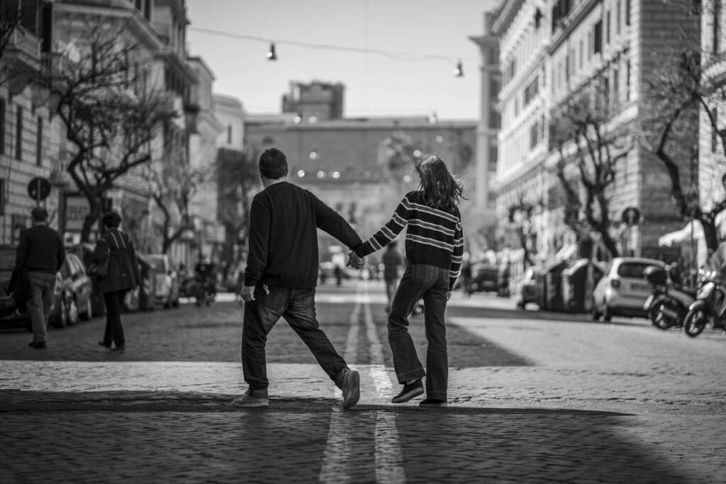 man and woman holding hands and crossing the road near people and vehicles during day