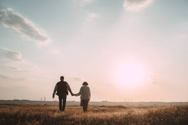 couple holding hands while walking on grass field during daytime